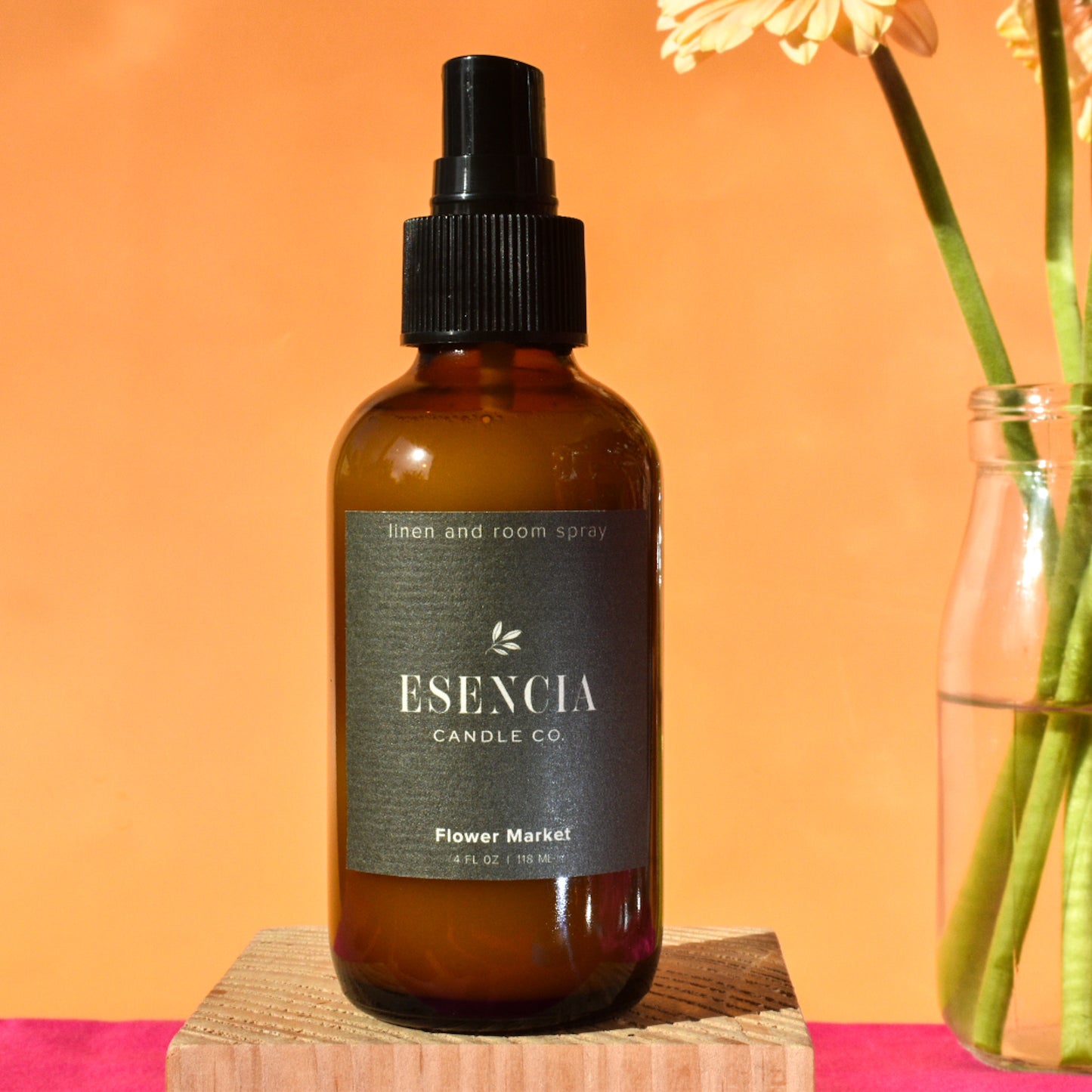 Brown spray bottle labeled 'Esencia Candle Co' on a wooden block with a pink background