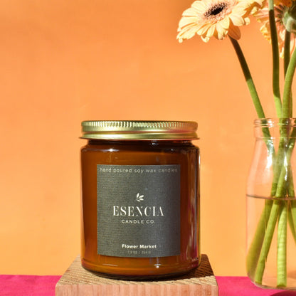 Esecia candle on a wooden block with flowers in the background