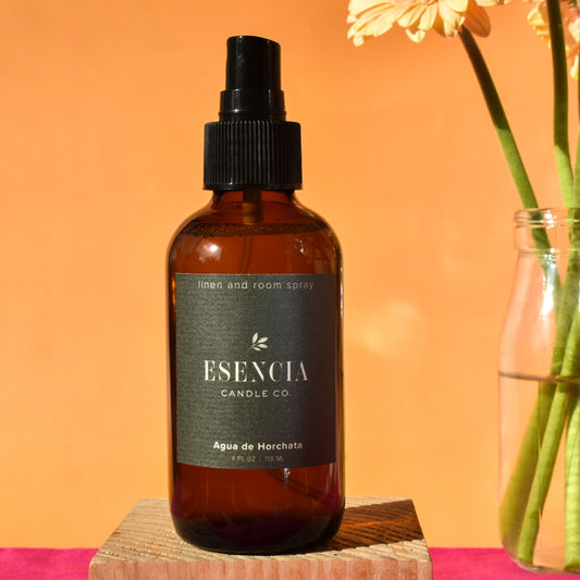Brown spray bottle with 'Esencia' label on a wooden block against an orange background
