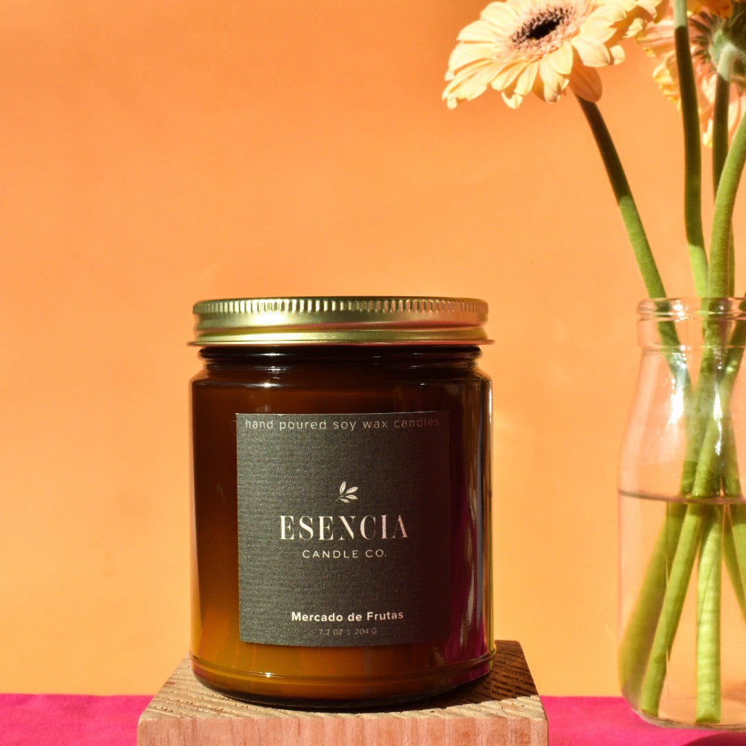 Jar of Esencia Candle Co. candle with a vase of flowers on an orange background