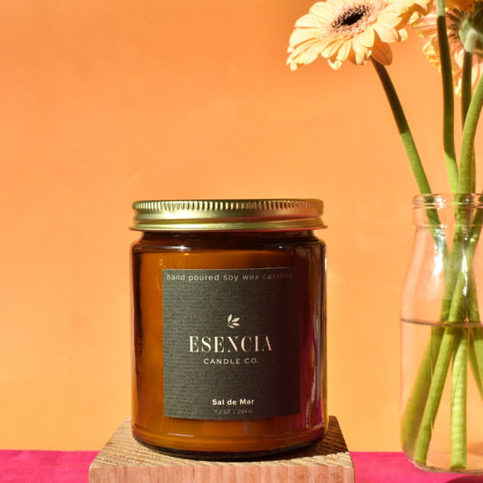 Esencia Candle Co. candle with a vase of flowers on an orange background