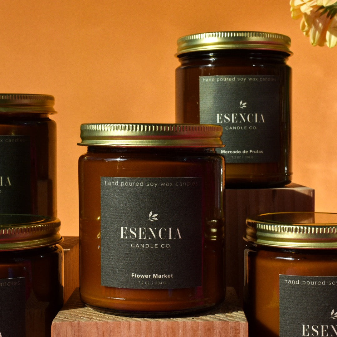 Esequia candle jars with labels on a wooden surface against an orange background